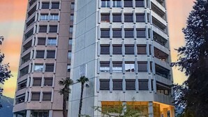Un hôtel de grande hauteur, avec de nombreux étages, une pelouse bien entretenue et une entrée bien visible, dotée d’un espace extérieur aménagé avec des sièges.