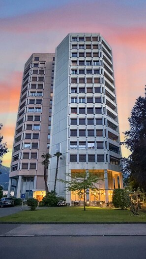 Ein Hochhaus-Hotel mit mehreren Etagen, einem gepflegten Rasen und einem Eingangsbereich mit Außenbestuhlung.