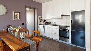 Une cuisine moderne avec des meubles blancs, un réfrigérateur en acier inoxydable et une table à manger en bois, assortie de chaises.