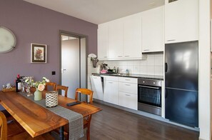 A modern kitchen with white cabinets, a stainless steel refrigerator, and a wooden dining table with chairs.
