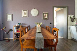 Una zona de menjador amb taula de fusta, cadires, un vas amb flors, obra d'art emmarcada a la paret i una petita estantàcia amb objectes decoratius.