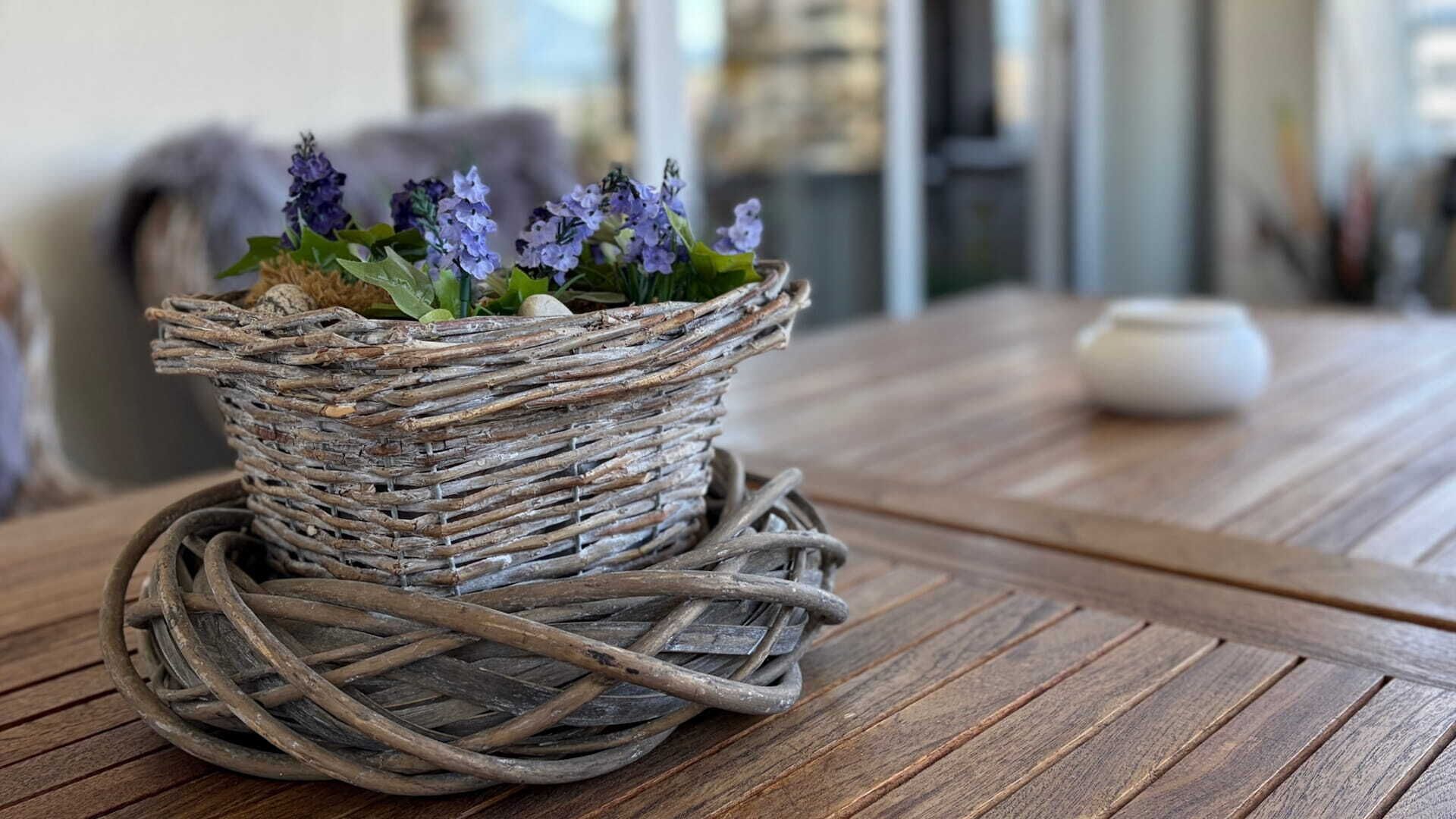 Un cesto di vimini con fiori su un tavolo di legno.