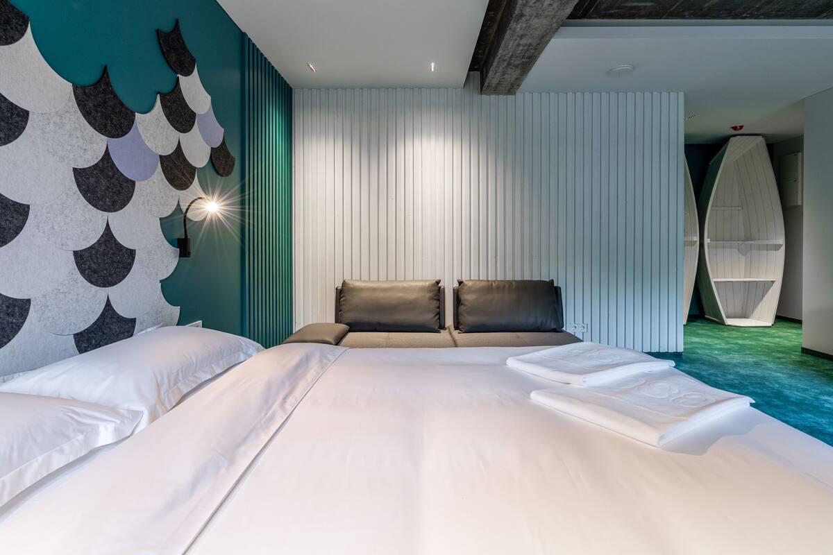 A modern hotel room with a large bed, a wall with a unique fish-scale design, and a ceiling with exposed beams.