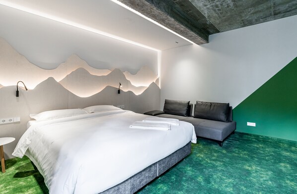 A modern bedroom with a large bed, a sofa, and a green carpet.