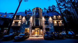 A multi-story hotel with a central glass tower, multiple balconies, and a parking area with cars. - ESE  Hotel (Birstonas)