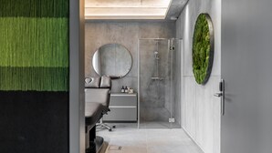 A modern bathroom with a glass shower, a round mirror, and a green moss wall.