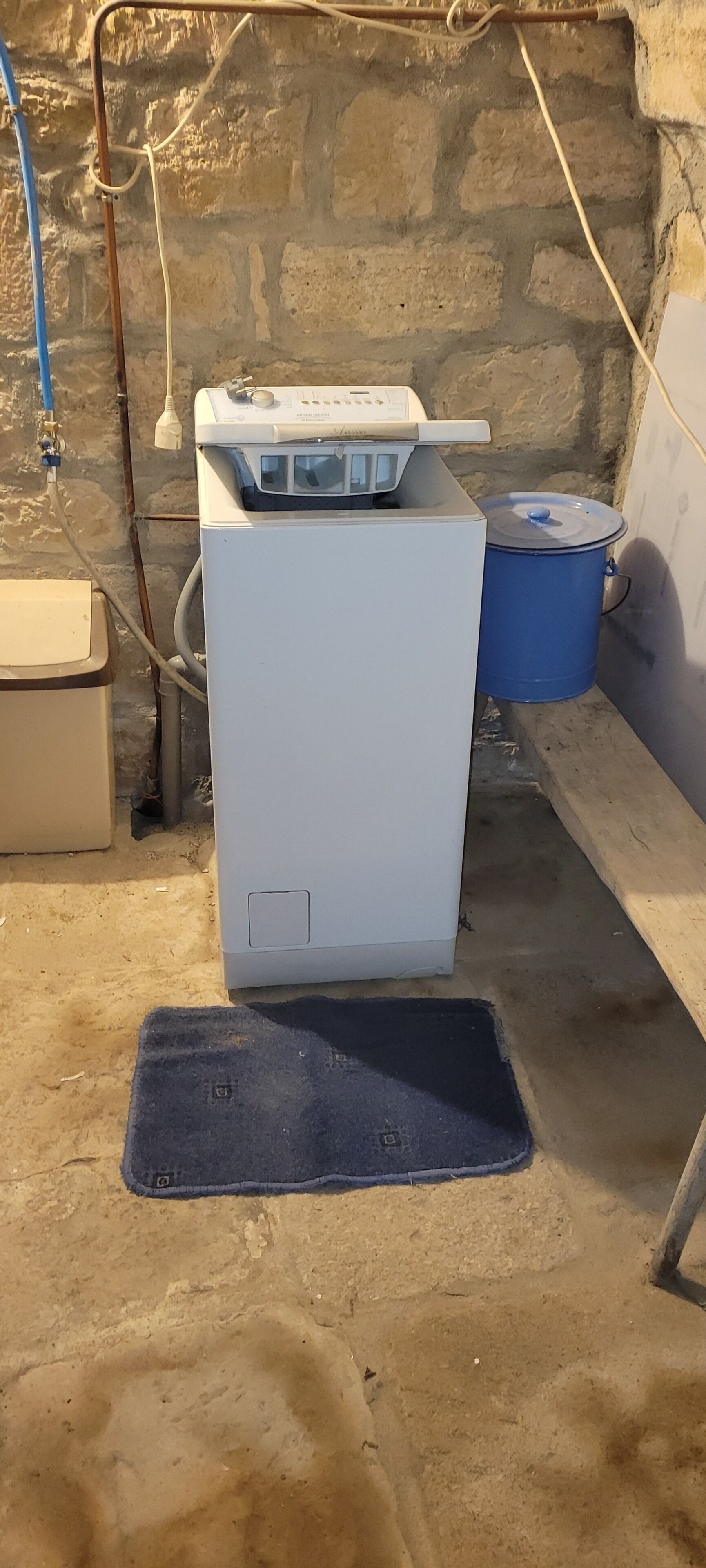 A compact room with a white appliance, a blue container, and a small mat on the floor.
