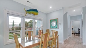 Uma sala de jantar com mesa de vidro, cadeiras de vime, uma grande decoração de peixe e vista pelas janelas.