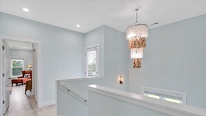 Um corredor amplo com escada, um lustre e vista para uma sala de jantar.