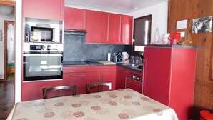 Una cocina compacta con armarios rojos, un microondas y una mesa de comedor con mantel estampado.