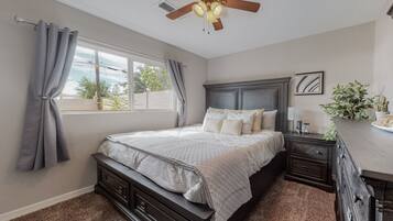 A bedroom with a bed, nightstands, a dresser, a ceiling fan, and a window with curtains.