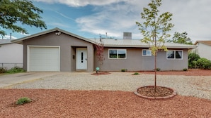 A single-story house with a garage, a small front yard with mulch and a tree, and a clear sky.