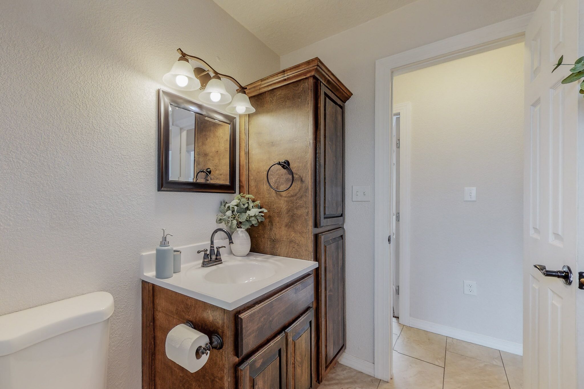 Un baño con tocador de madera, espejo, lavamanos y retrete.