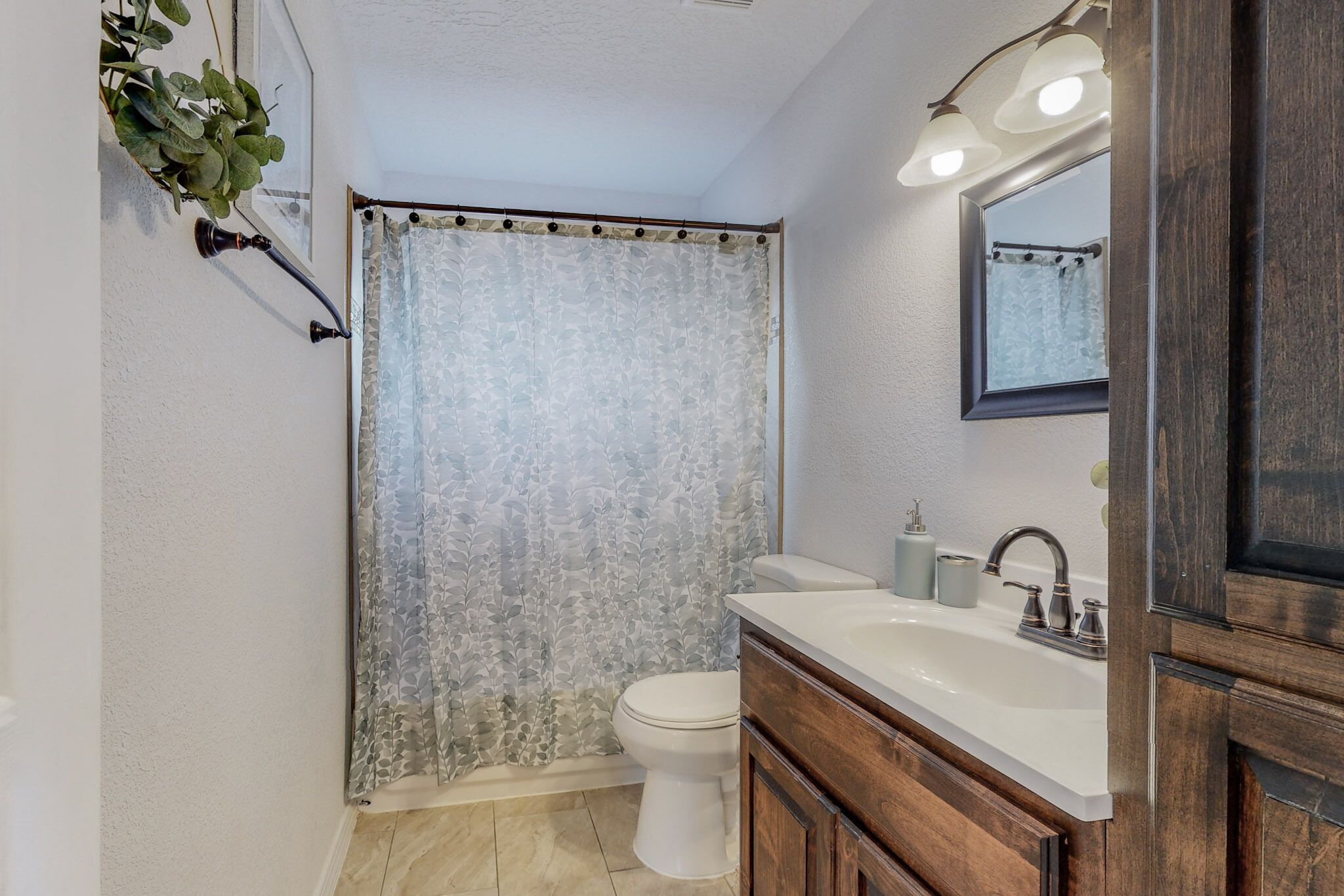 A bathroom with a shower curtain, toilet, sink, and mirror.