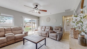 A spacious living room with a ceiling fan, two beige sofas, a wooden coffee table, and a large window.