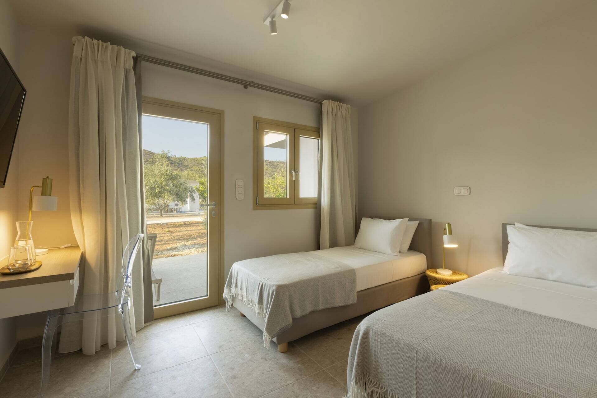 A hotel room with two beds, a desk, and a chair. There are curtains, a window, and a view of the outdoors.