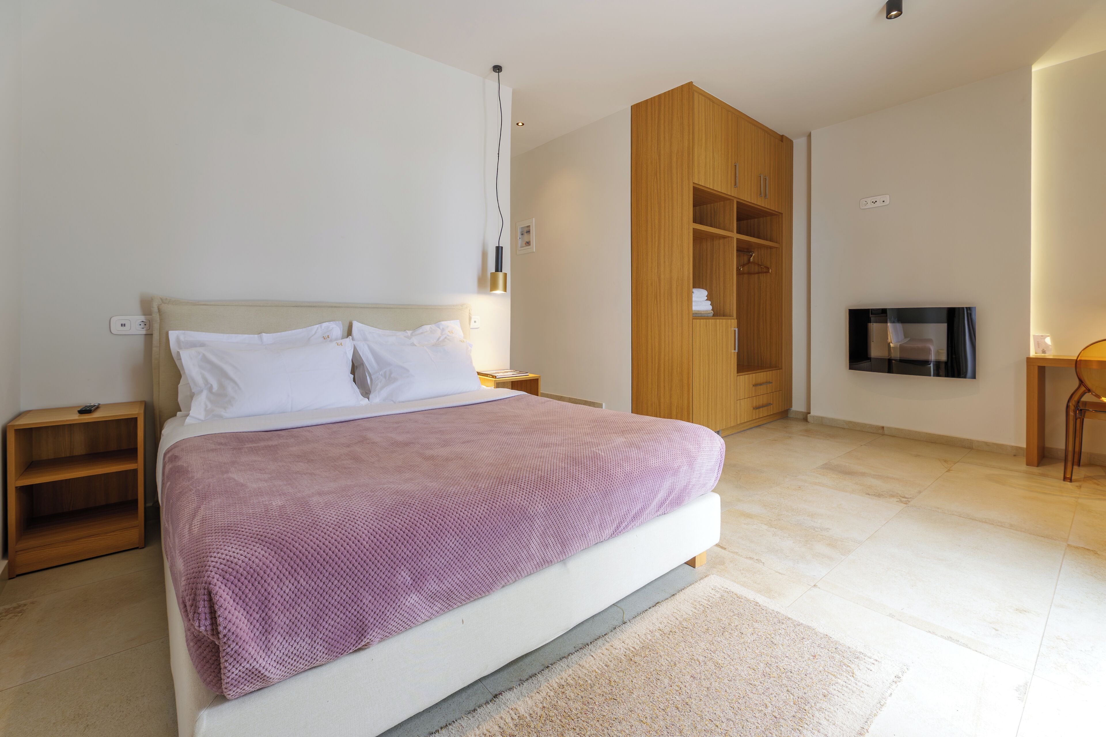 A modern bedroom with a large bed, wooden wardrobe, and a TV mounted on the wall.