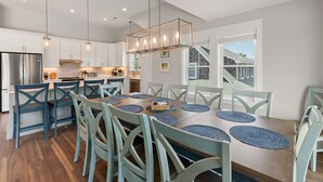 Een moderne keuken met witte kasten, een roestvrijstalen koelkast en een eethoek met een houten tafel en blauwe stoelen.
