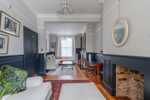 A living room with a fireplace, a sofa, a coffee table, and a dining area with a table and chairs. - Stylish 2 Bedroom Home in Islington With Garden (London)