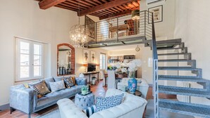 A spacious living area with a high ceiling and exposed wooden beams, a staircase with metal railings, and a view of the kitchen in the background. - Casa Lucky, Romantic Modern 3 bedrooms Penthouse inside the Walls of Lucca (Lucca)