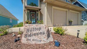 En stenskil med texten ”Hilltop Hideaway 206 Hilltop” står framför ett hus med ett garage och en uppfart.