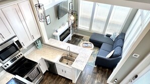 Una cocina moderna con una isla central, un rincón de comedor con sofá, y una escalera que sube a un nivel superior.