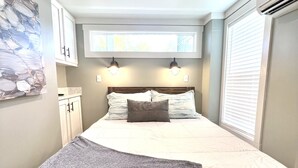 Un dormitorio con una cama, lámparas de noche, una ventana con persianas y un aire acondicionado de pared.