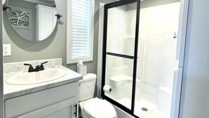 Un baño con lavamanos blanco, inodoro y ducha con mampara de vidrio.