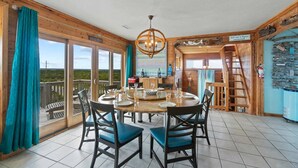 A dining area with a round table, chairs, and a chandelier. - Oceanfront Home w/ Private Pool, Hot Tub, Private Beach Boardwalk. It's the One! (Avon)