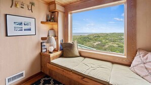 A cozy corner with a built-in bench, a framed photo, a lamp, and a view of a green landscape. - Oceanfront Home w/ Private Pool, Hot Tub, Private Beach Boardwalk. It's the One! (Avon)