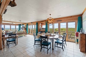 Une pièce spacieuse avec une grande table à manger, des chaises et une vue sur le paysage grâce à de grandes fenêtres.