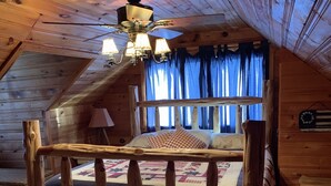 Un dormitorio rústico de cabaña con estructura de cama de madera, ventilador de techo y ventana con cortinas azules.