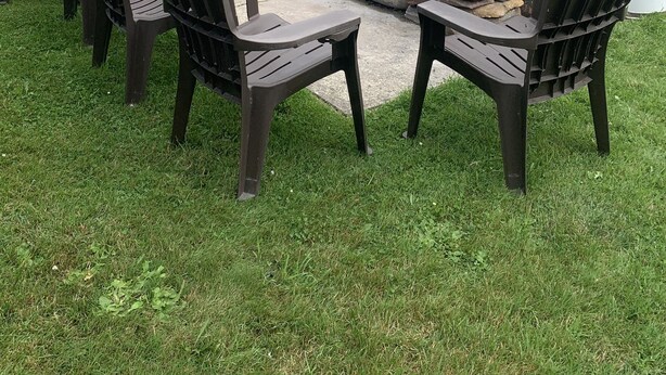 Un espacio al aire libre con sillas Adirondack y un hogar de piedra junto a un lago.