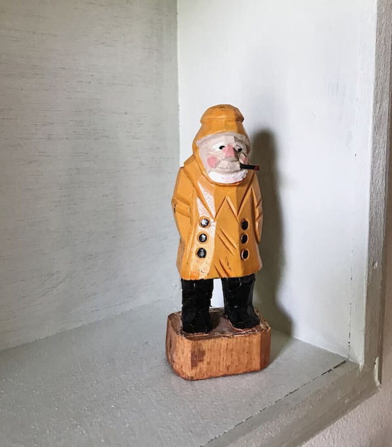 En træfigur af en karakter i en gul frakke og hat, stående på en træsokkel.