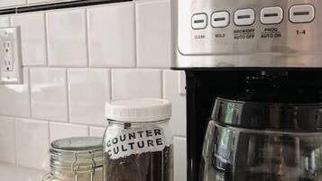 Une cuisine avec une machine à café Cuisinart, un bocal étiqueté « COUNTER CULTURE » et une assiette sur laquelle se trouve un petit bocal.