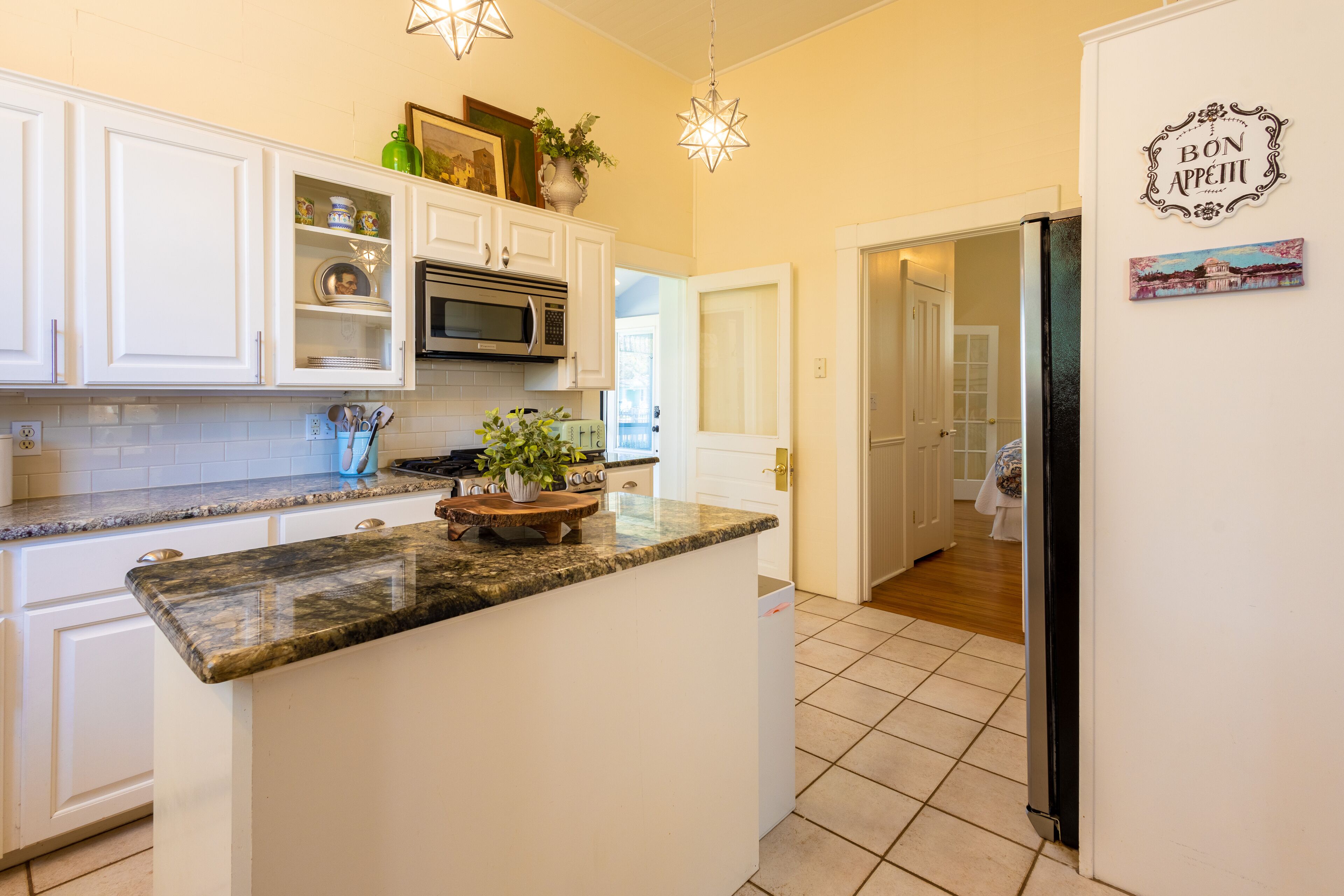A kitchen with white cabinets, a granite countertop, a microwave, and a refrigerator.