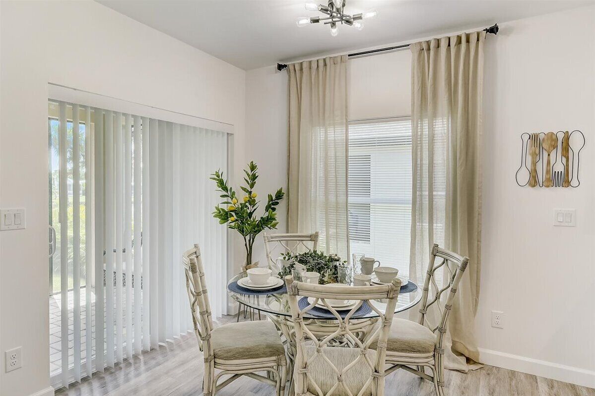 A dining area with a round table, white chairs, and a vase with flowers.