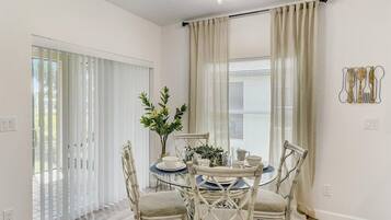 A dining area with a round table, white chairs, and a vase with flowers.
