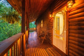 A wooden cabin with a porch, a door with a glass panel, and a view of greenery.