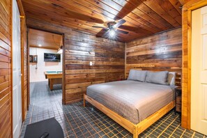 A wooden cabin room with a bed, a ceiling fan, a clock, and a television. - Fern Ridge Cabin - Hot Tub - 60 Acres with Trails! (Laurelville)