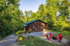 Un chalet rustique avec un toit végétalisé, entouré d’une végétation luxuriante et doté d’une allée en gravier.
