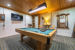 Une table de billard avec une boule blanche, une table de billard et un téléviseur fixé au mur.