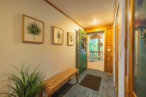A hallway with framed botanical prints, a bench, a potted plant, and a wooden door leading to a balcony. - Fern Ridge Cabin - Hot Tub - 60 Acres with Trails! (Laurelville)