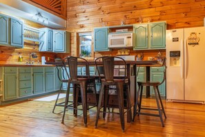 Une cuisine avec des meubles en bois, une table à manger avec des chaises, un réfrigérateur et un four à micro-ondes.