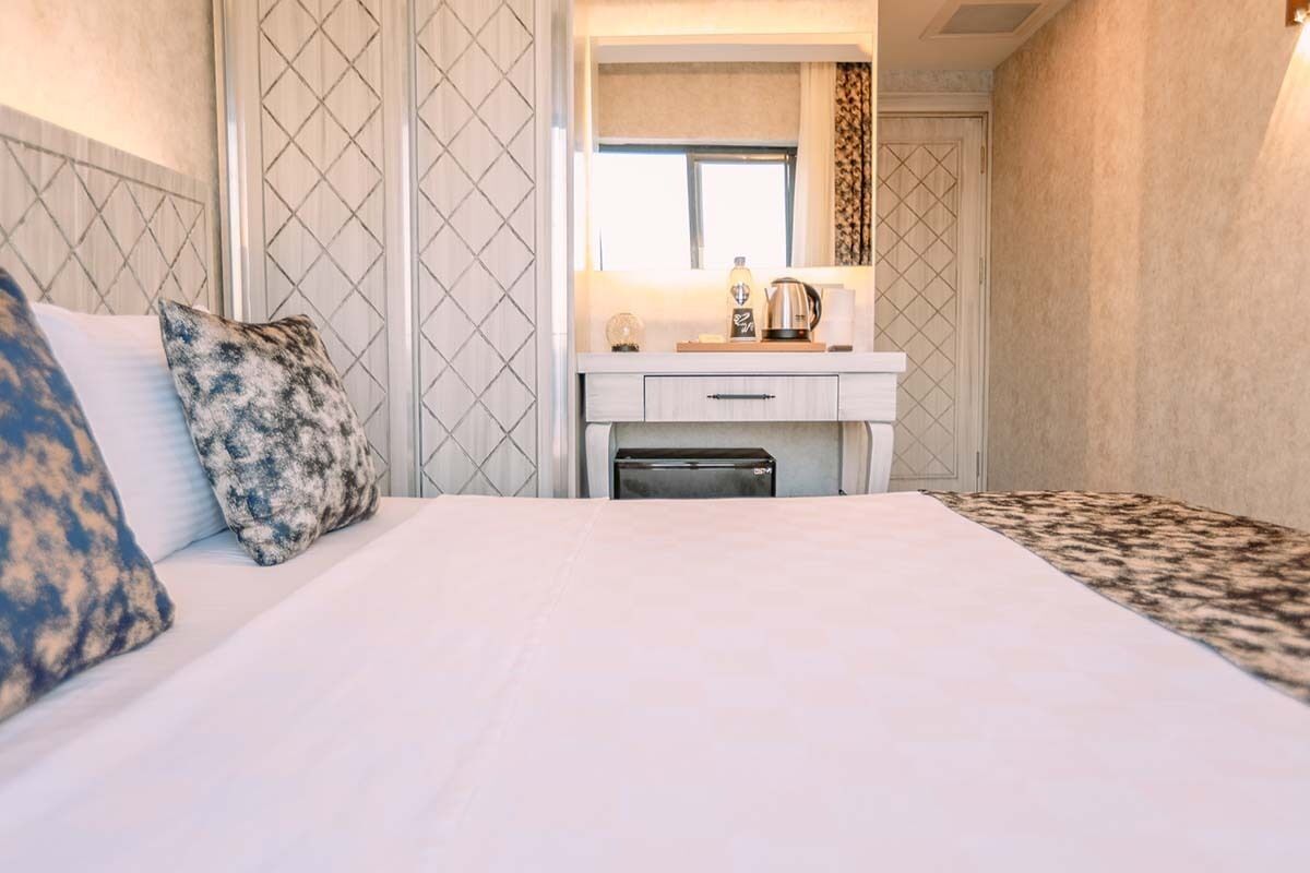 Habitación de hotel con una cama, una mesita de noche con lámpara, un espejo y una ventana.