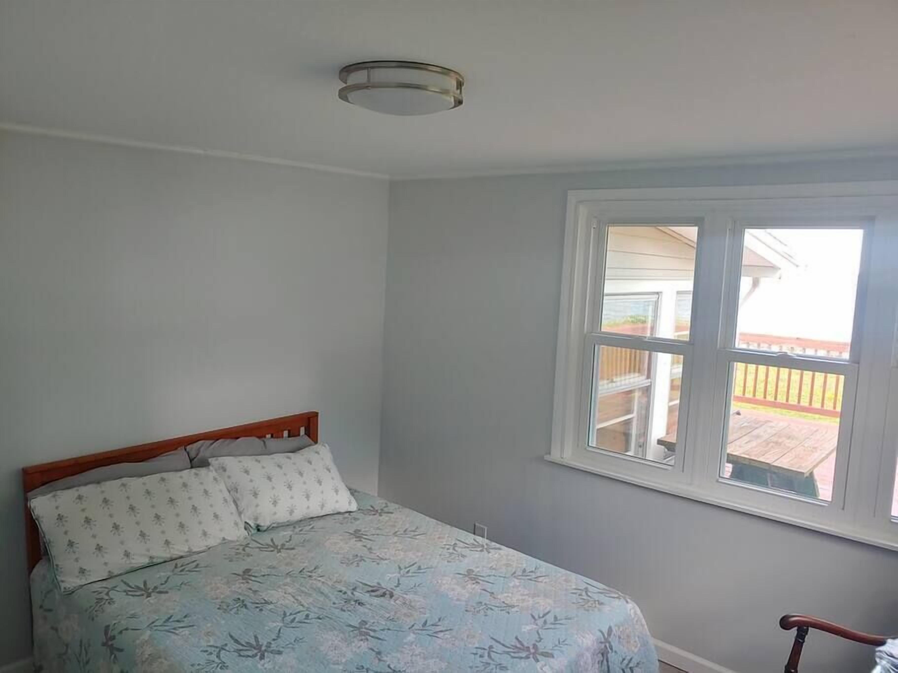 Een slaapkamer met een bed, een raam en een plafondlamp.