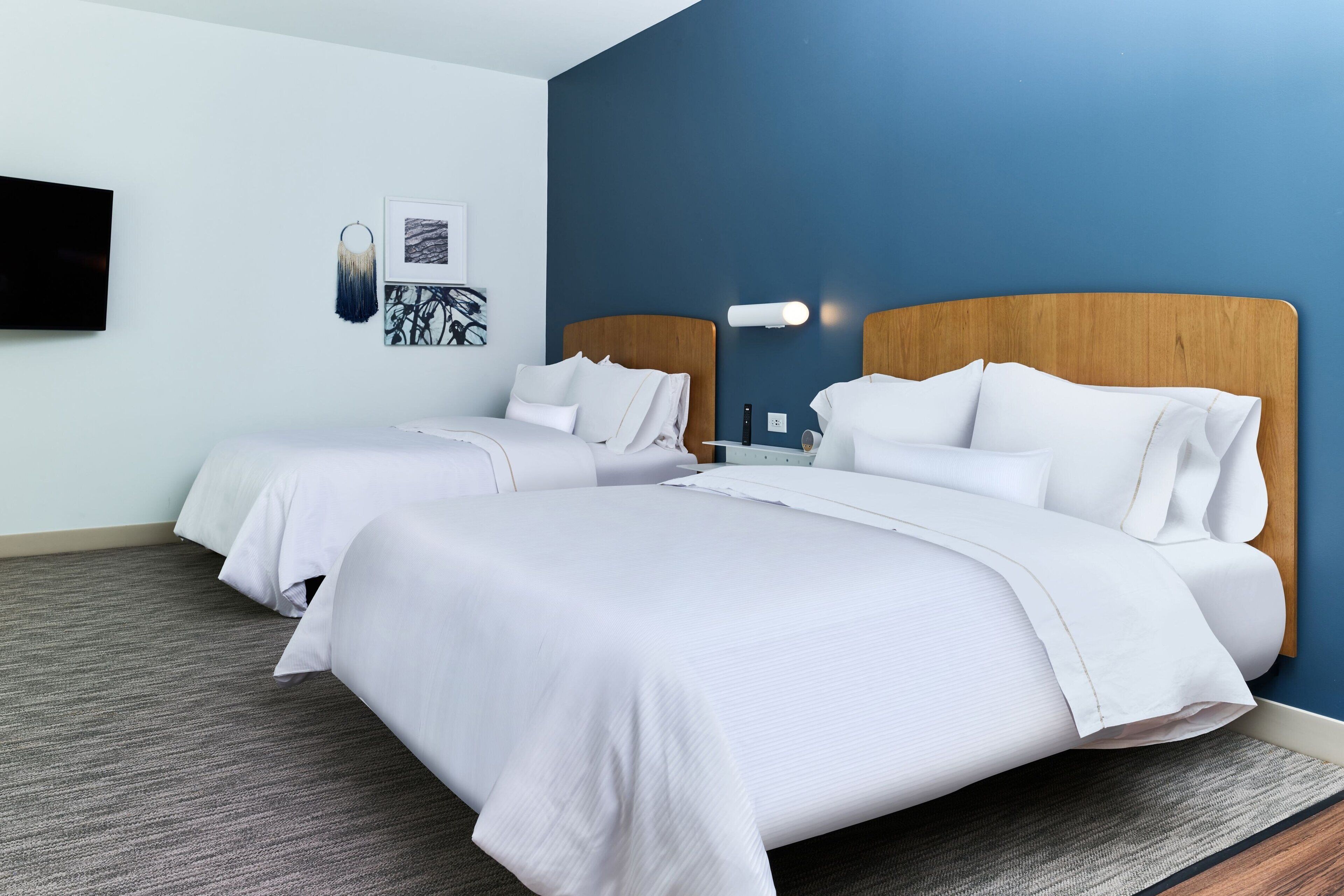 A hotel room with two beds, a flat-screen TV mounted on the wall, and a framed artwork above the beds.