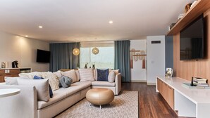 Ein modernes Wohnzimmer mit einer Eckcouch, einem runden Hocker, einem kleinen runden Tisch und einer eingebauten TV-Konsole.