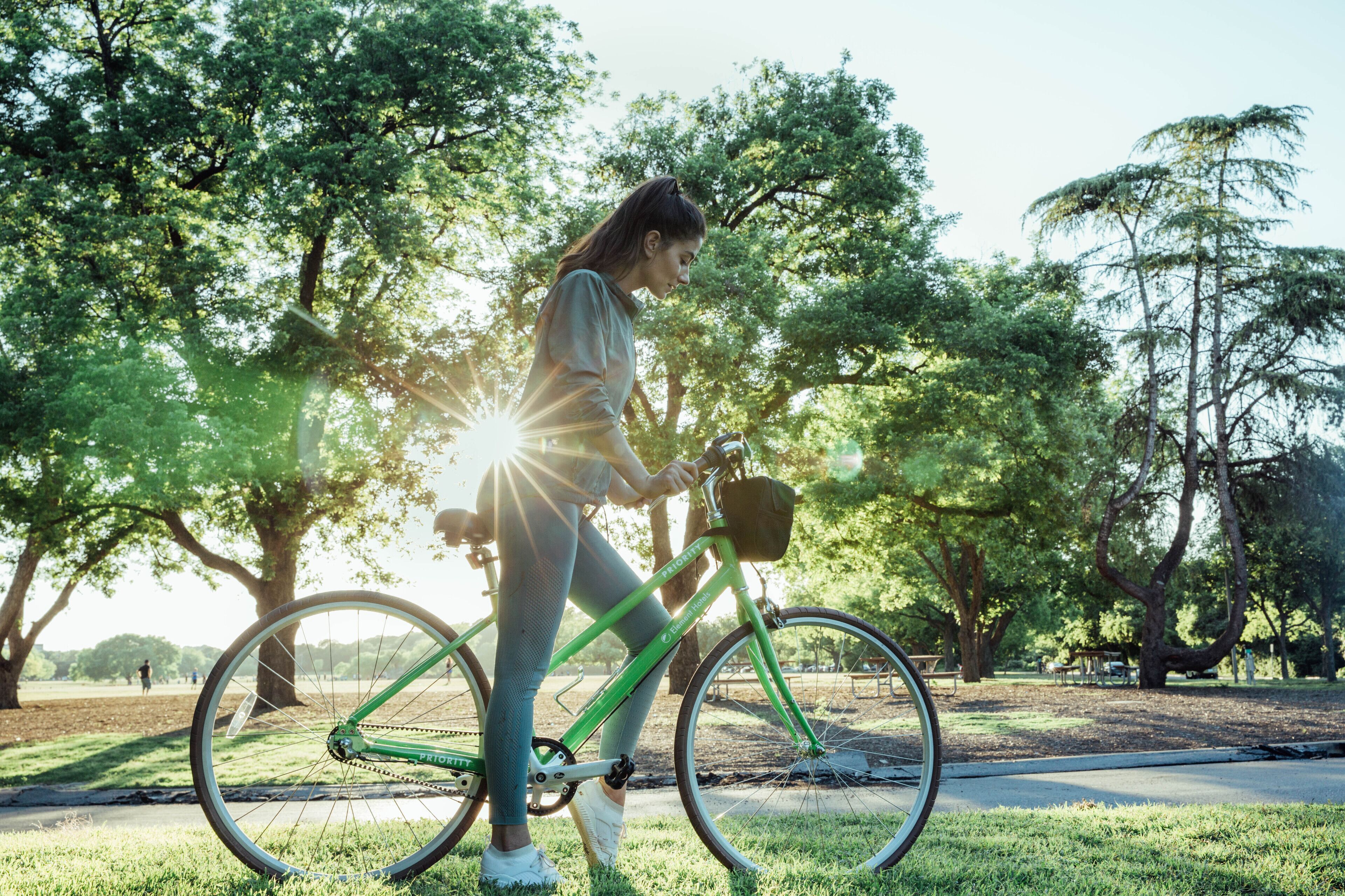 A person riding a green bicycle in a park with trees and a bench in the background.
