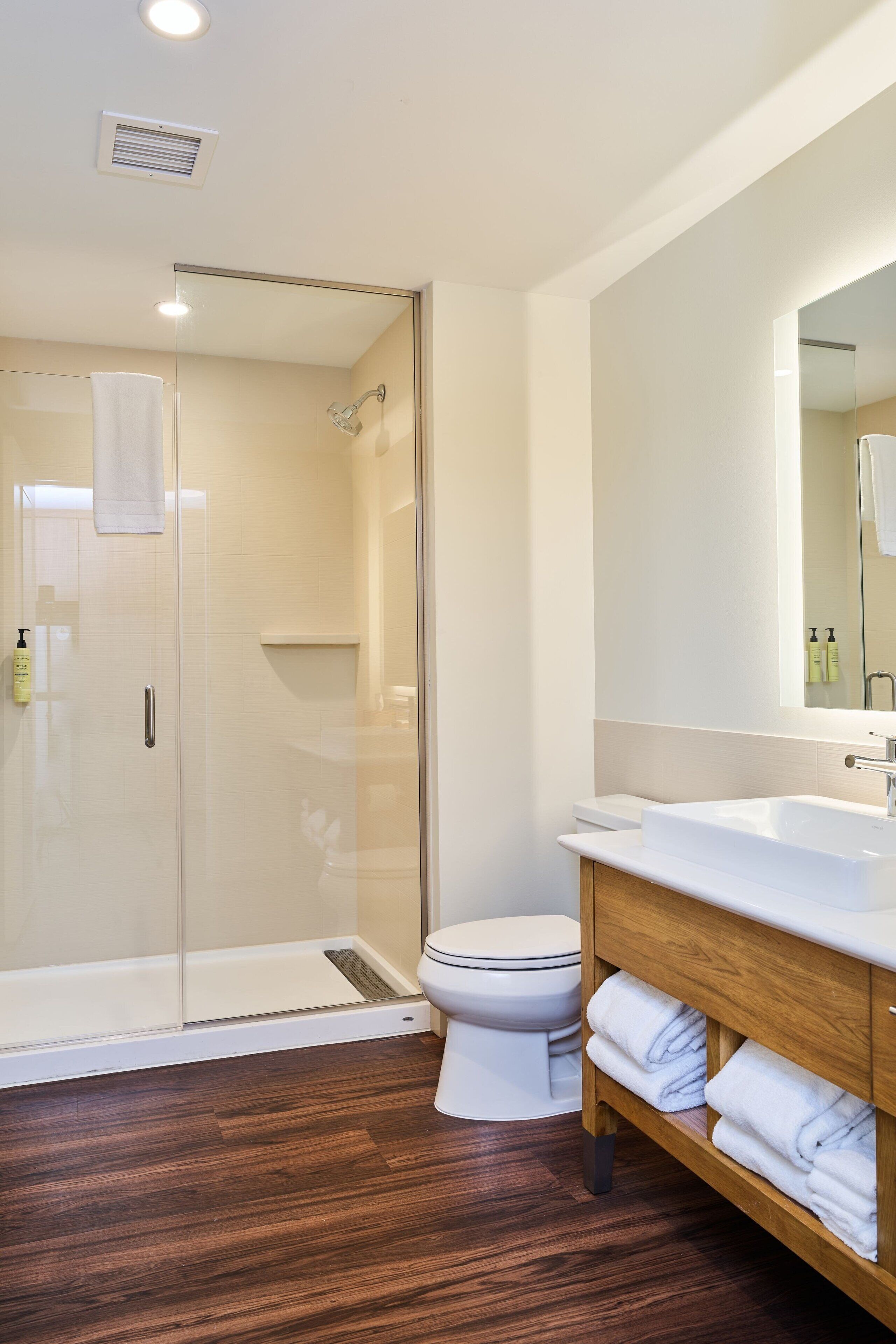 A modern bathroom with a glass shower enclosure, a white toilet, and a wooden vanity with a mirror.